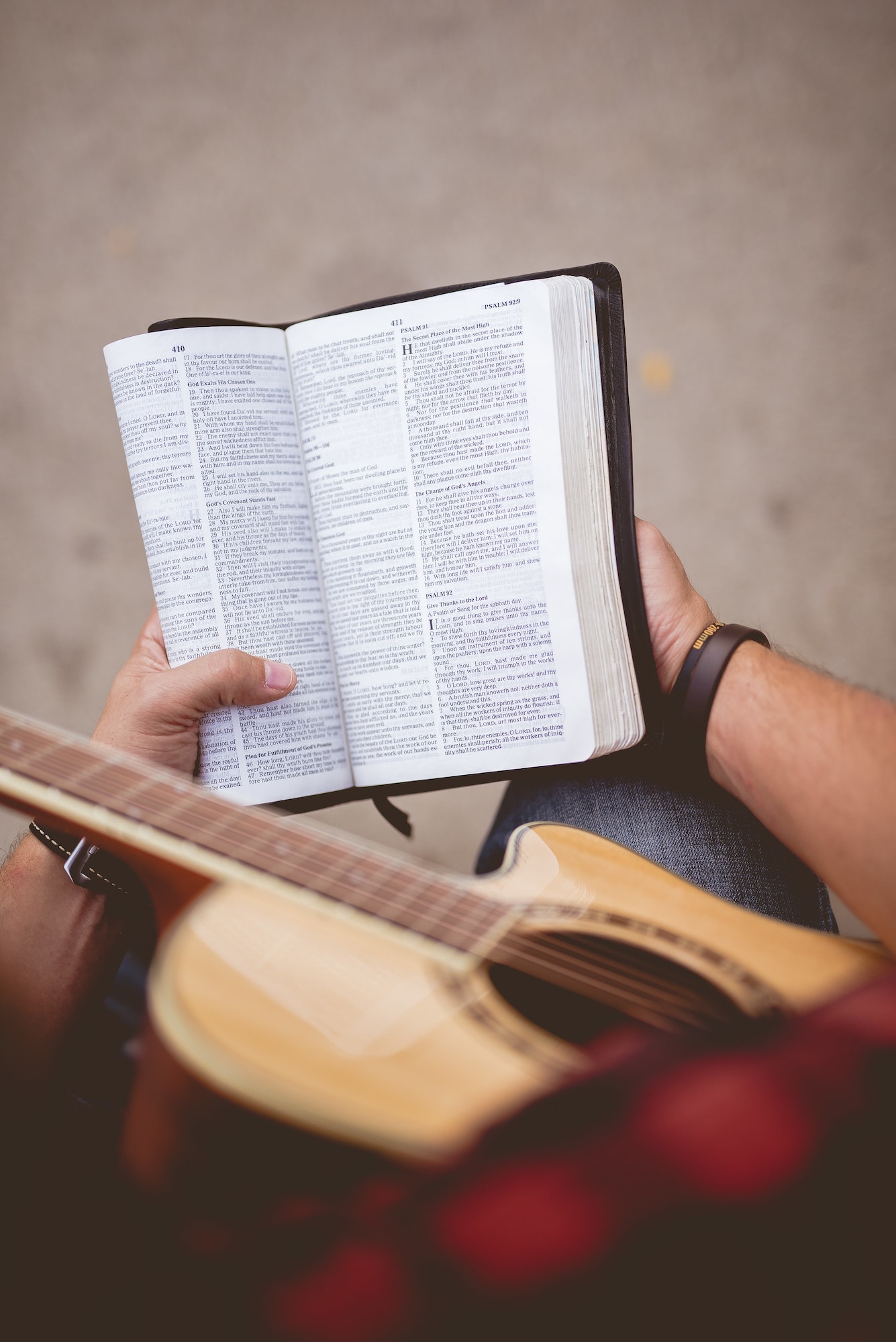 Overhead vertical shot of a person sitting with his guitar and reading a bible